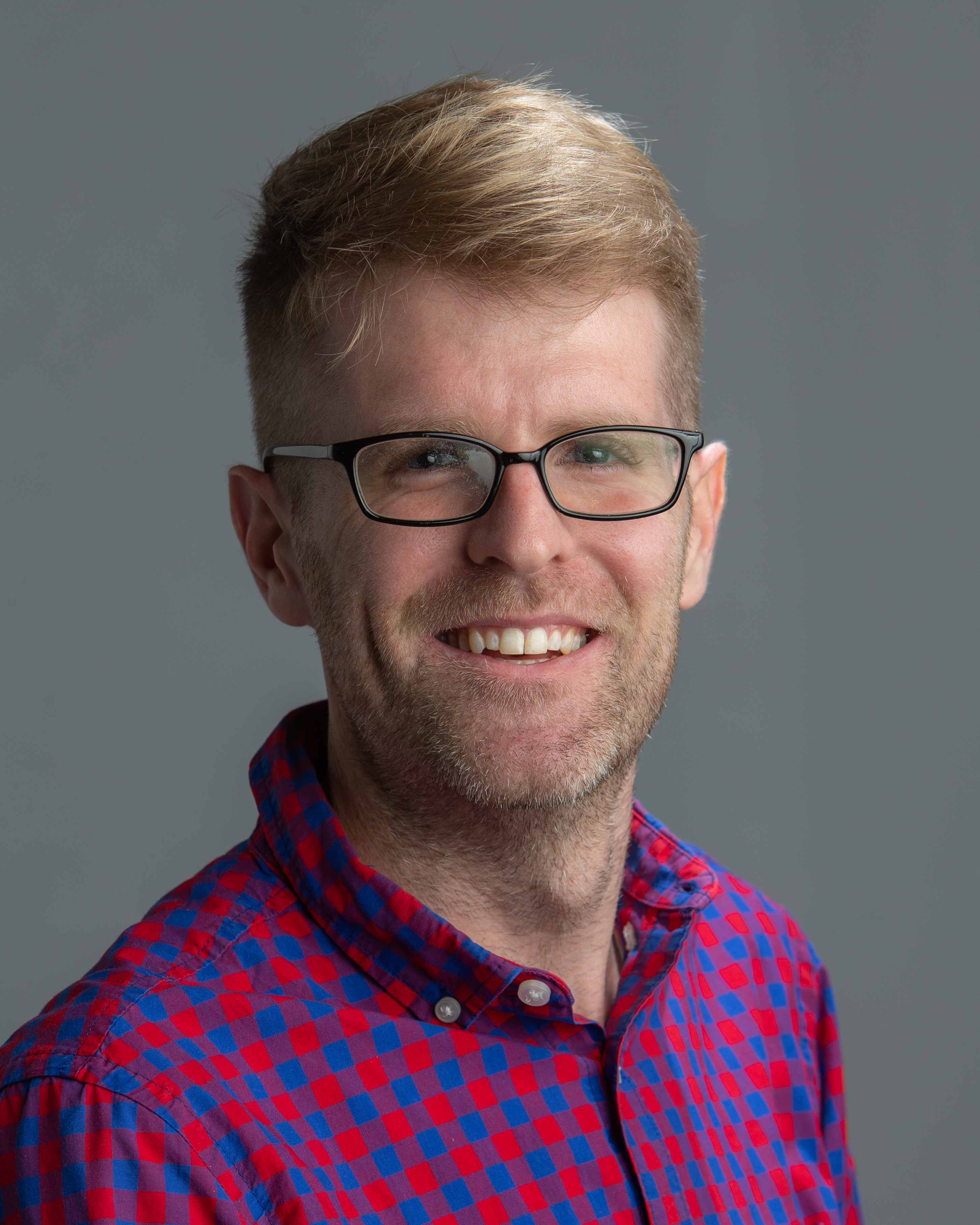 Tim Keogh headshot, blonde male wearing glasses and plaid shirt