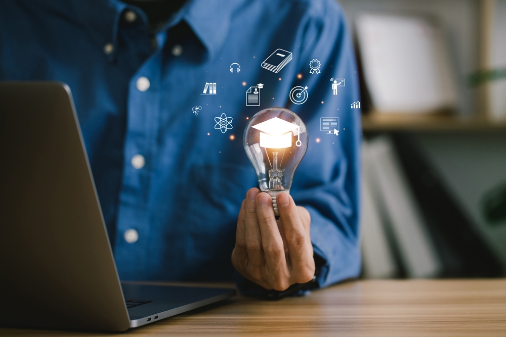 male with laptop holding lightbulb with floating graphics of graduation cap