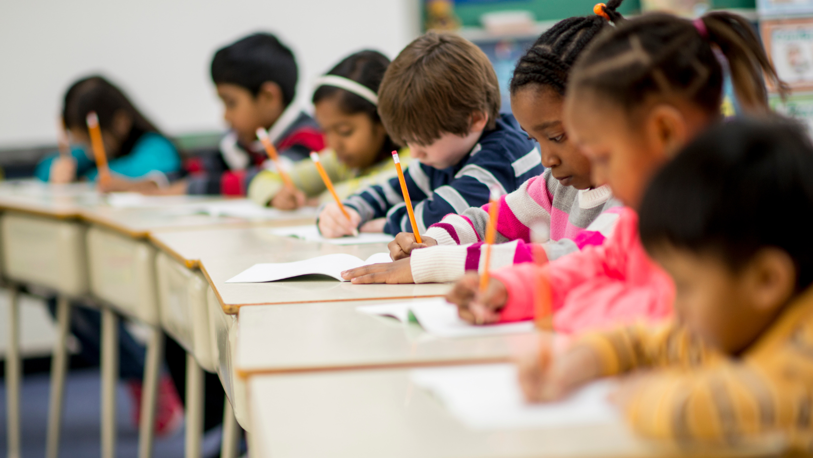 Child writing on paper with teacher looking over shoulder.