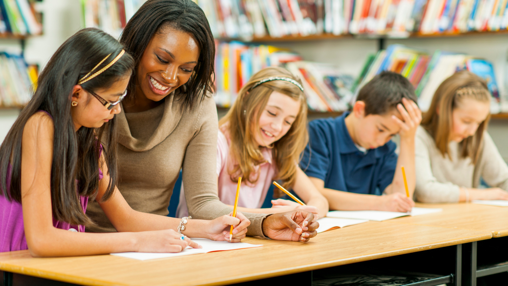 Child writing on paper with teacher looking over shoulder.