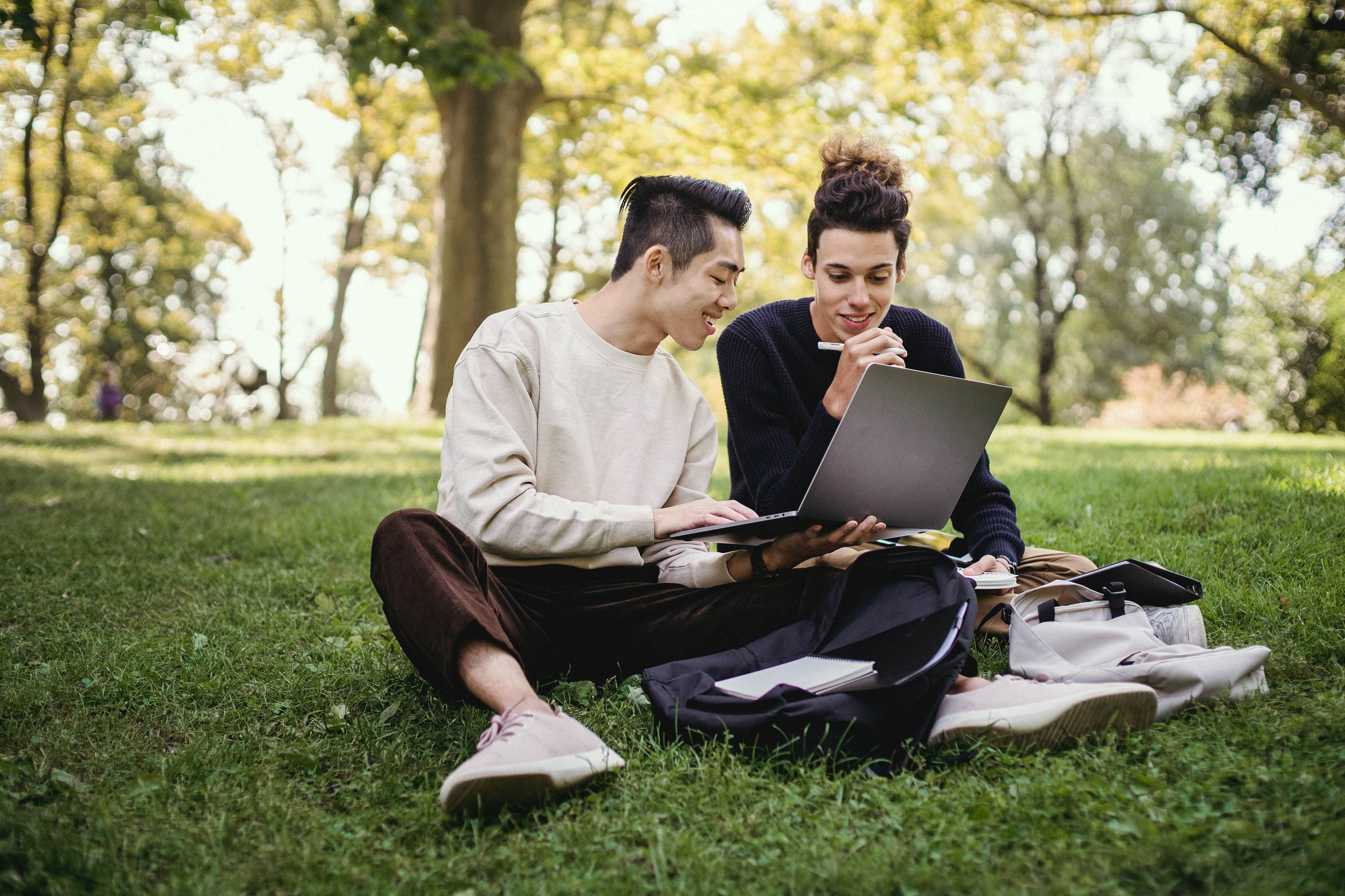 Two college students sitting in grass working on a laptop