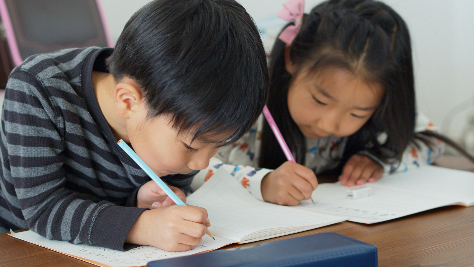 Child writing on paper with teacher looking over shoulder.