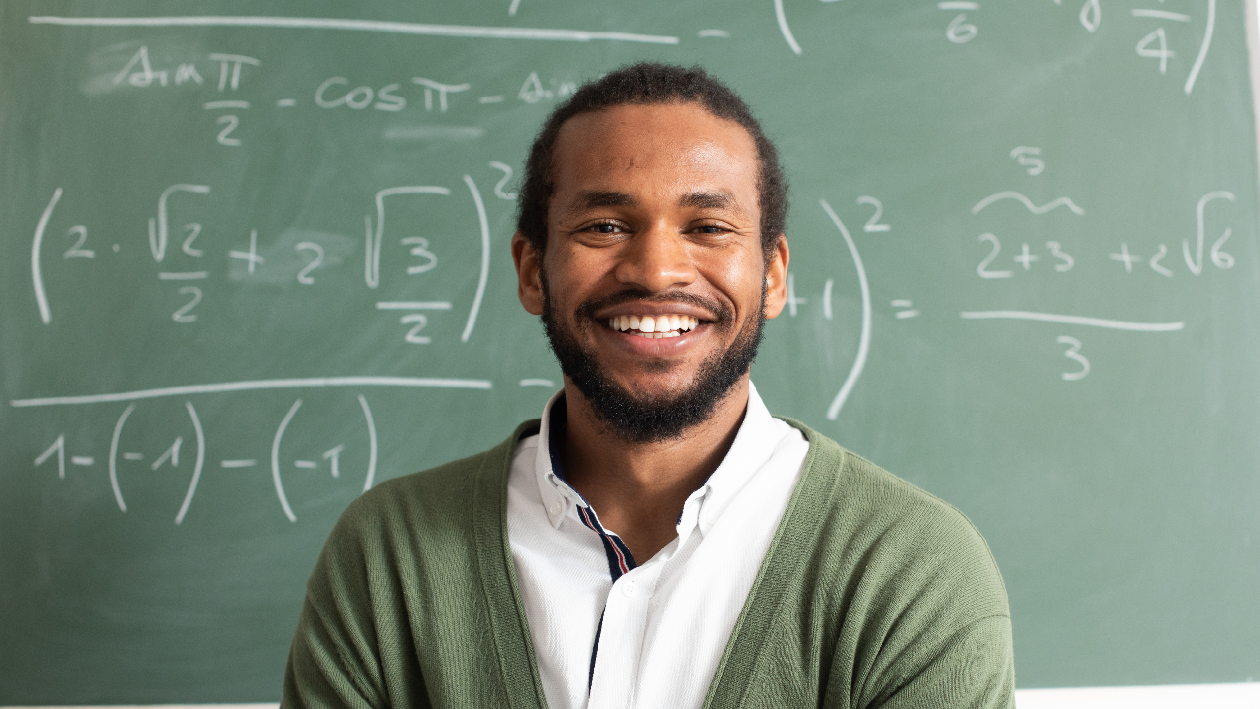 Black male teacher standing in front of a chalkboard smiling