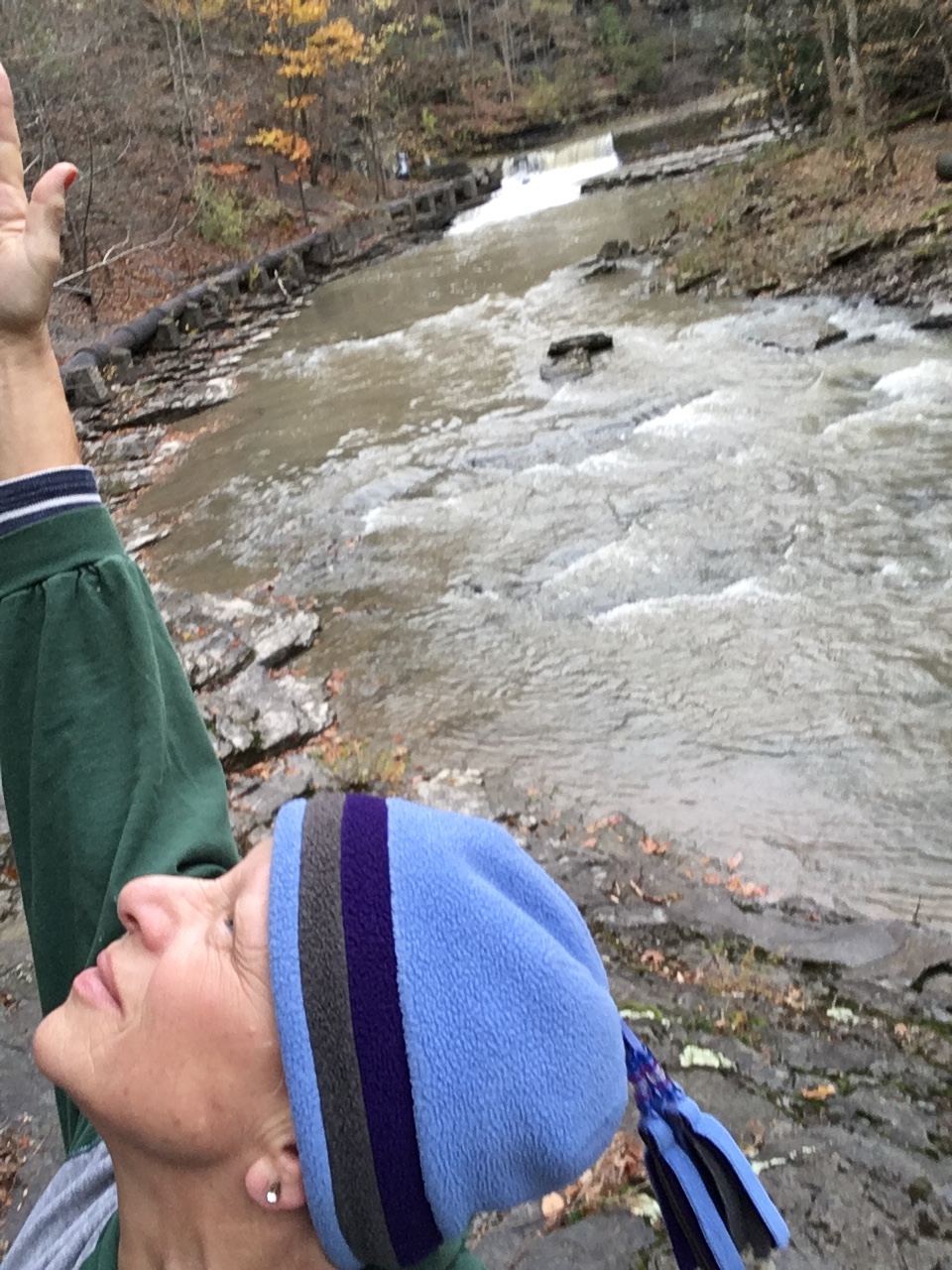 Carrie Stern raising her hand and looking up, as the river flows behind her