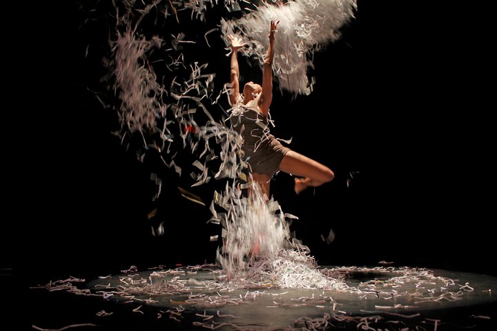 Professor Nicole McClam dancing on stage, lifting paper shreds everywhere