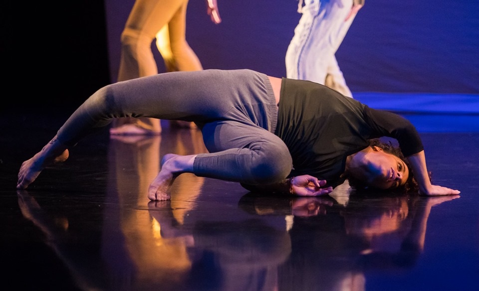 female dancer in green long sleeve shirt and grey leggings, on the ground