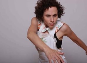 Professor Aviva Geismar wearing a floral white dress with both her arms outstretched to her left, where she is also gazing