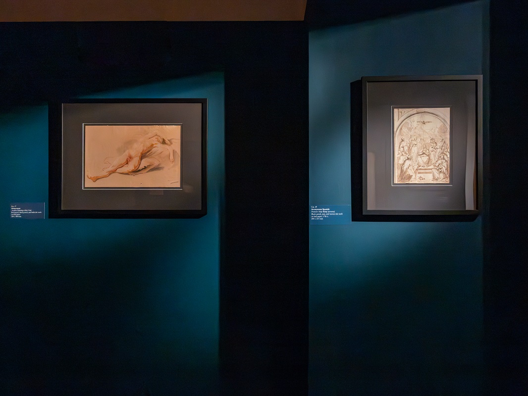 Two paintings hanging on a dark room's wall.