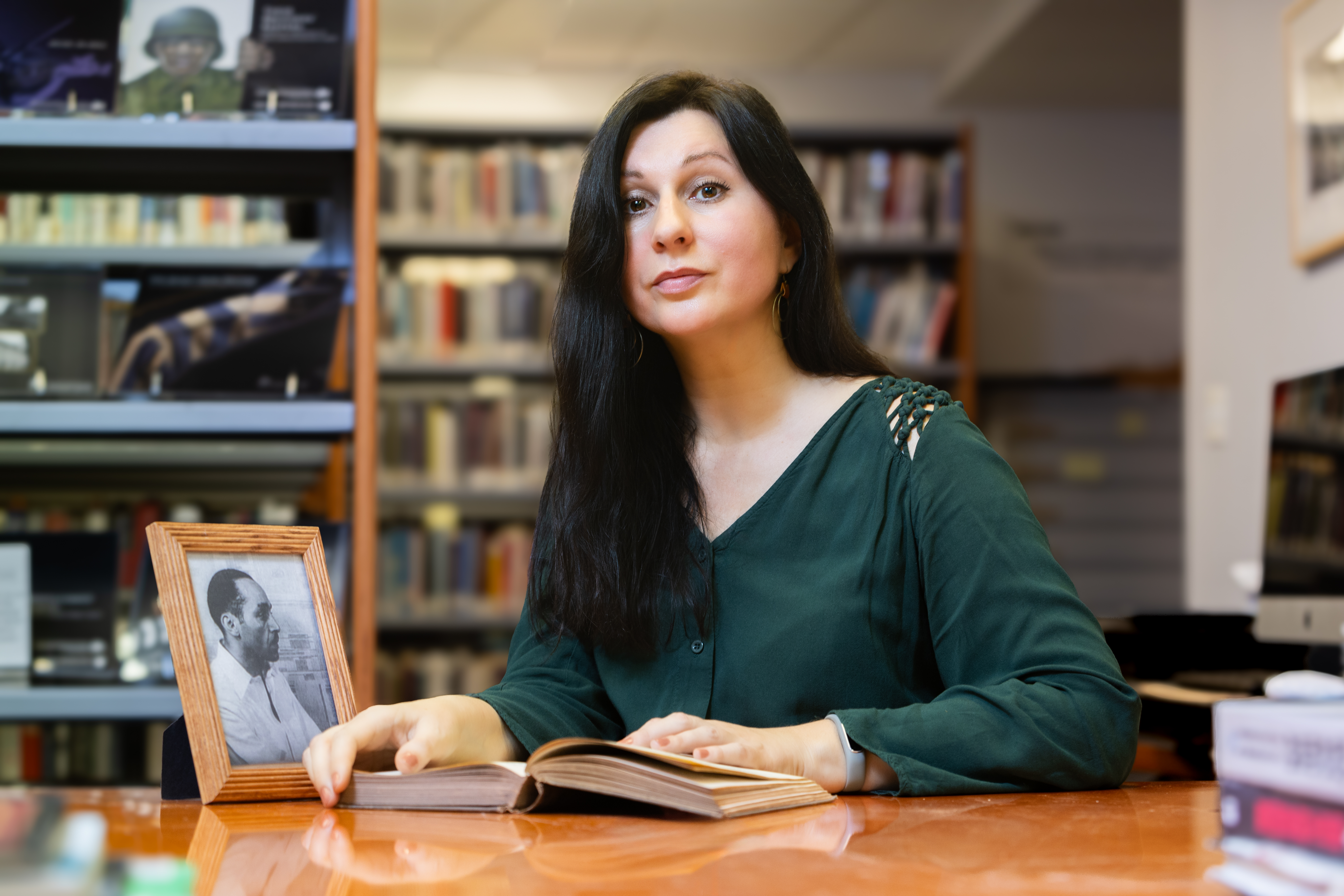 Agnieszka Tuszynska in a library with a book in hand and framed photo 